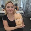 Smiling lash student with a practice mannequin head
