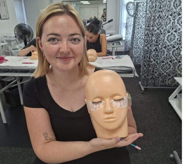 Smiling lash student with a practice mannequin head