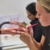 Students practising acrylic nail extensions on practice hands