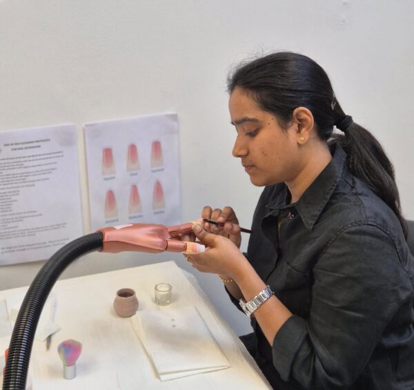 Student applying acrylic nail extensions to a practice hand