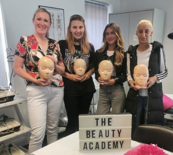Smiling lash students holding practice mannequin heads