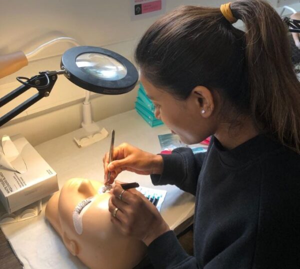 Student practising lash extensions under a magnifying lamp