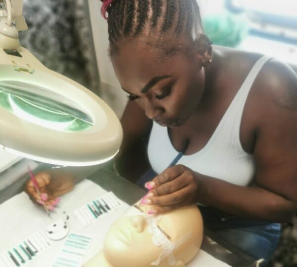 Student practising lash extensions under a magnifying lamp
