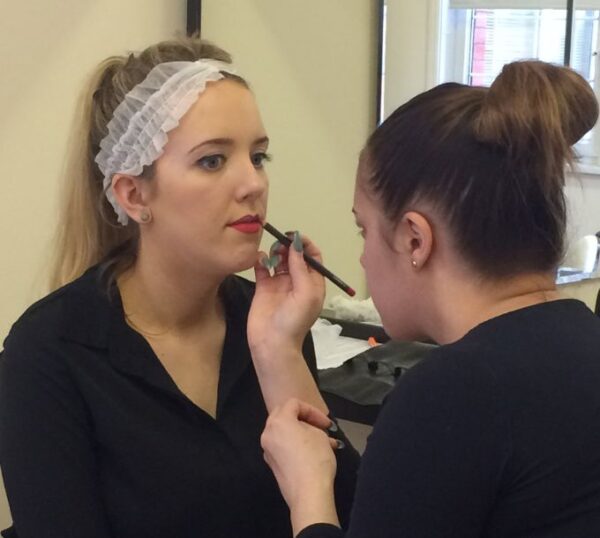 Student applying lip liner to a model