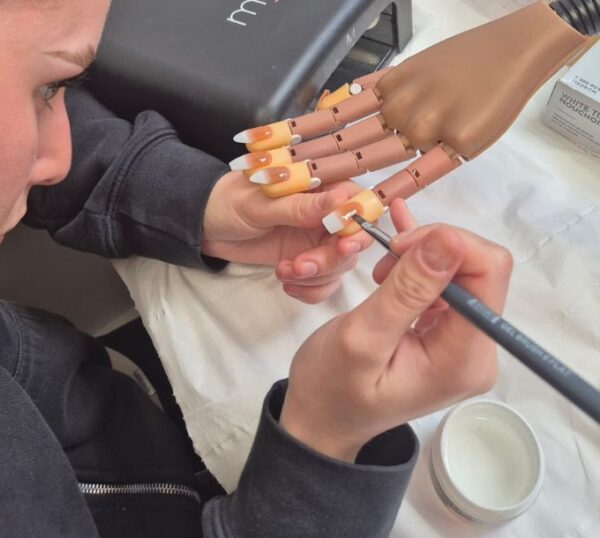 Student painting gel polish on a practice hand
