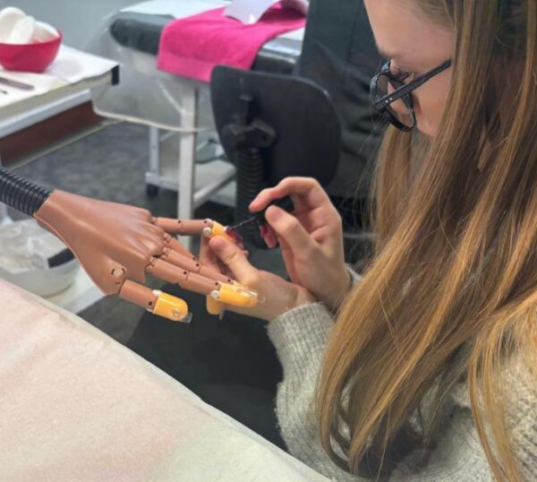 Student applying nail extensions to a practice hand