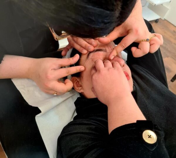 Student shaping brows with tweezers
